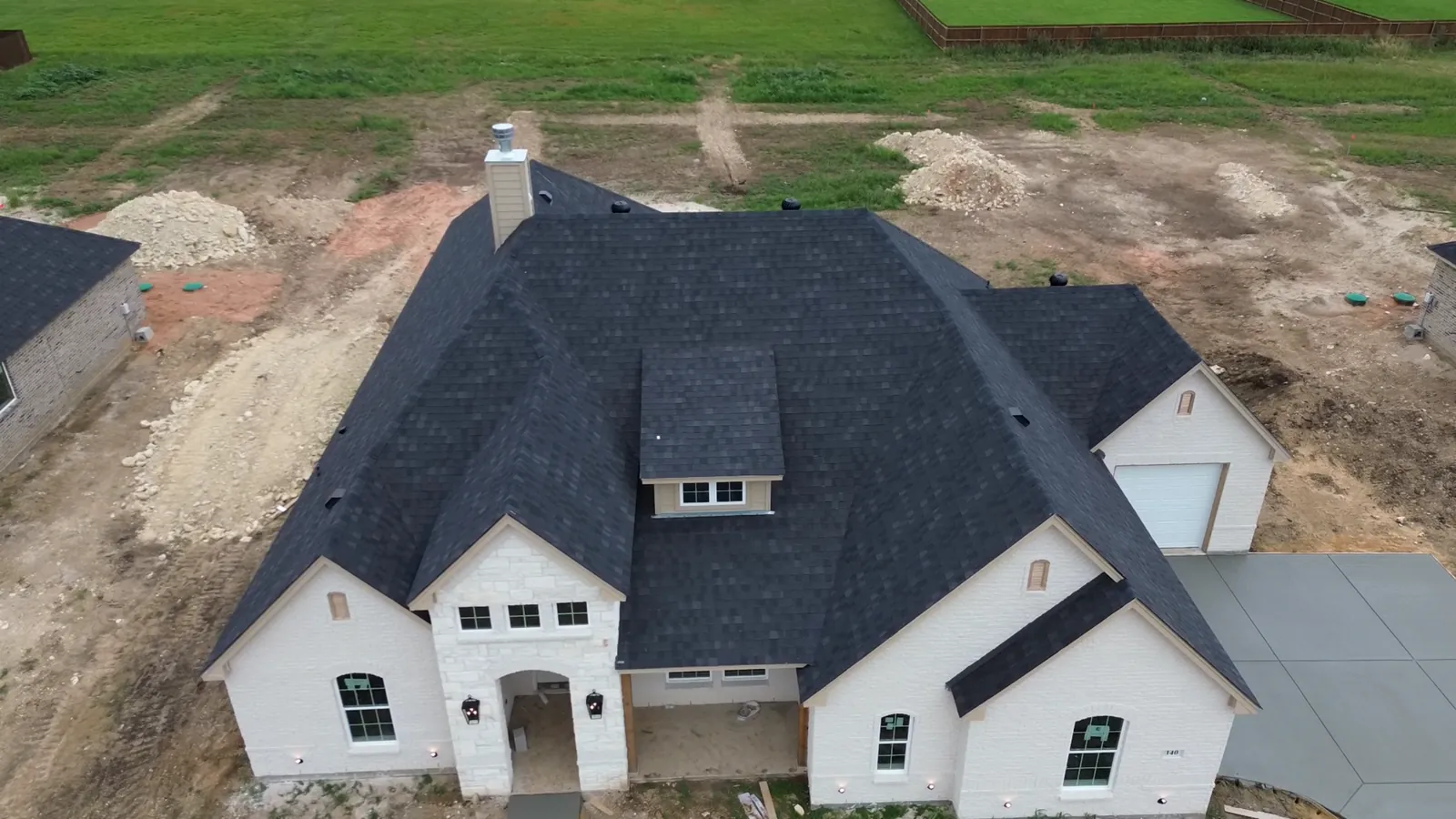 Aerial view of a finished dark shingle roof on a newly built stone home